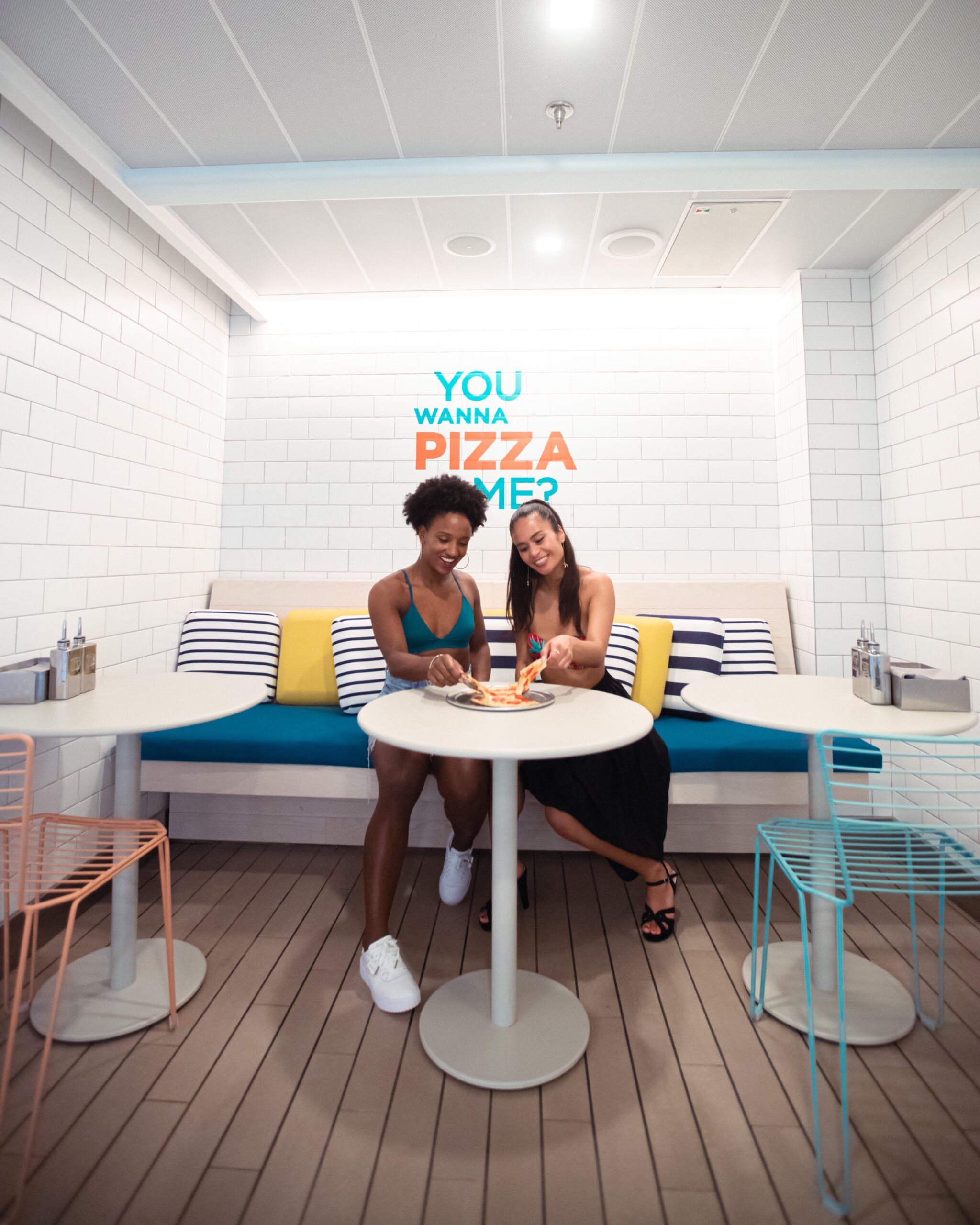 Two women enjoying pizza in front of the You Want A Pizza Me sign at The Pizza Place. @ginajoyphoto