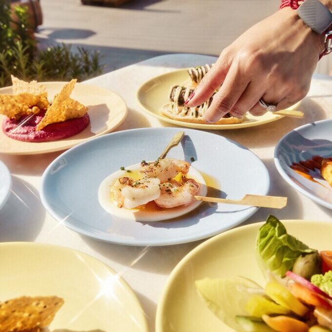 A hand reaches for food from The Dock House on a table. 

Now We're Voyaging Campaign
Photographer: Alberto Oviedo
Studio: Christian Schrader, Kathy Boos
Brand: Billy Bohan